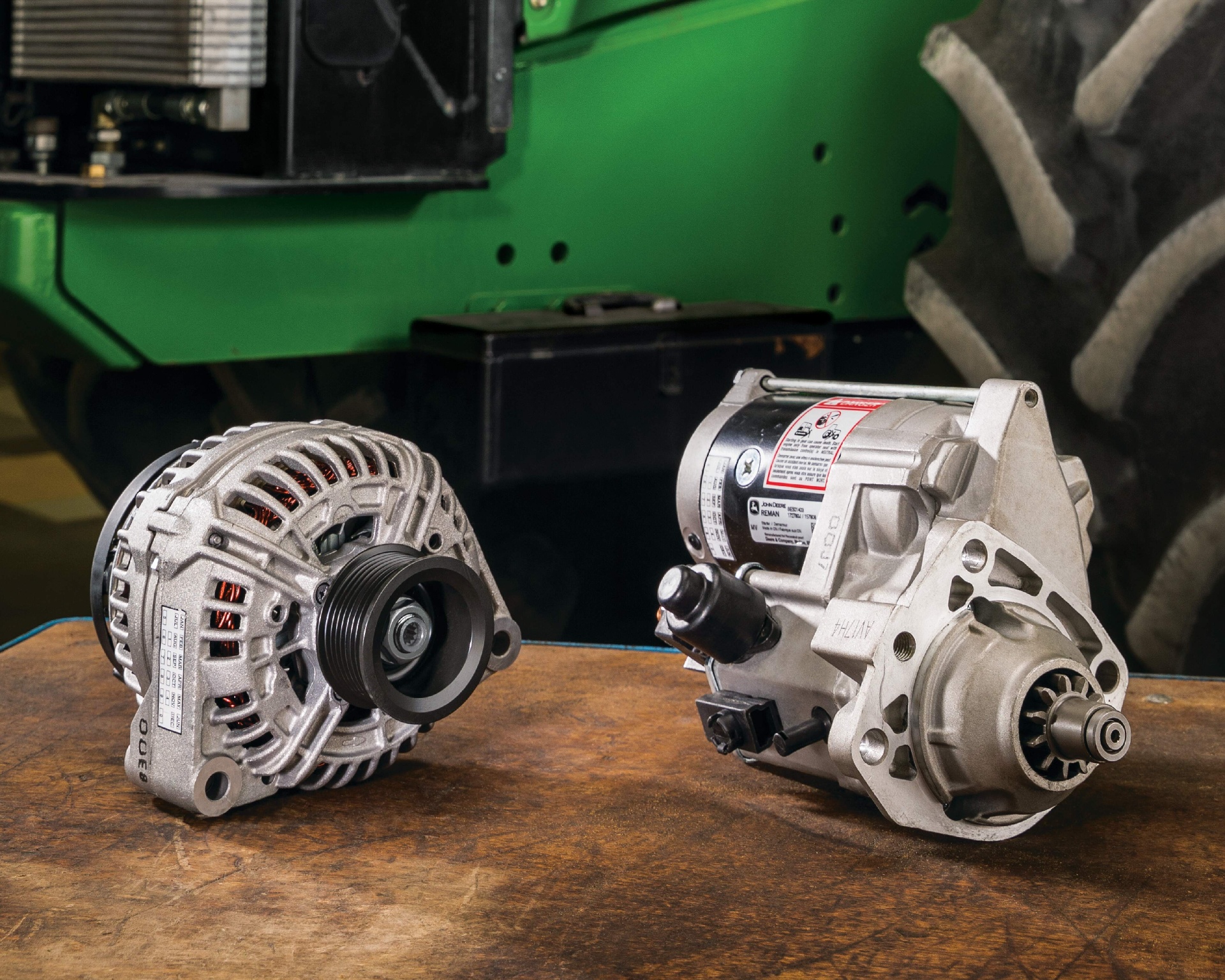 John Deere Reman alternator and starter on a workbench in front of a tractor
