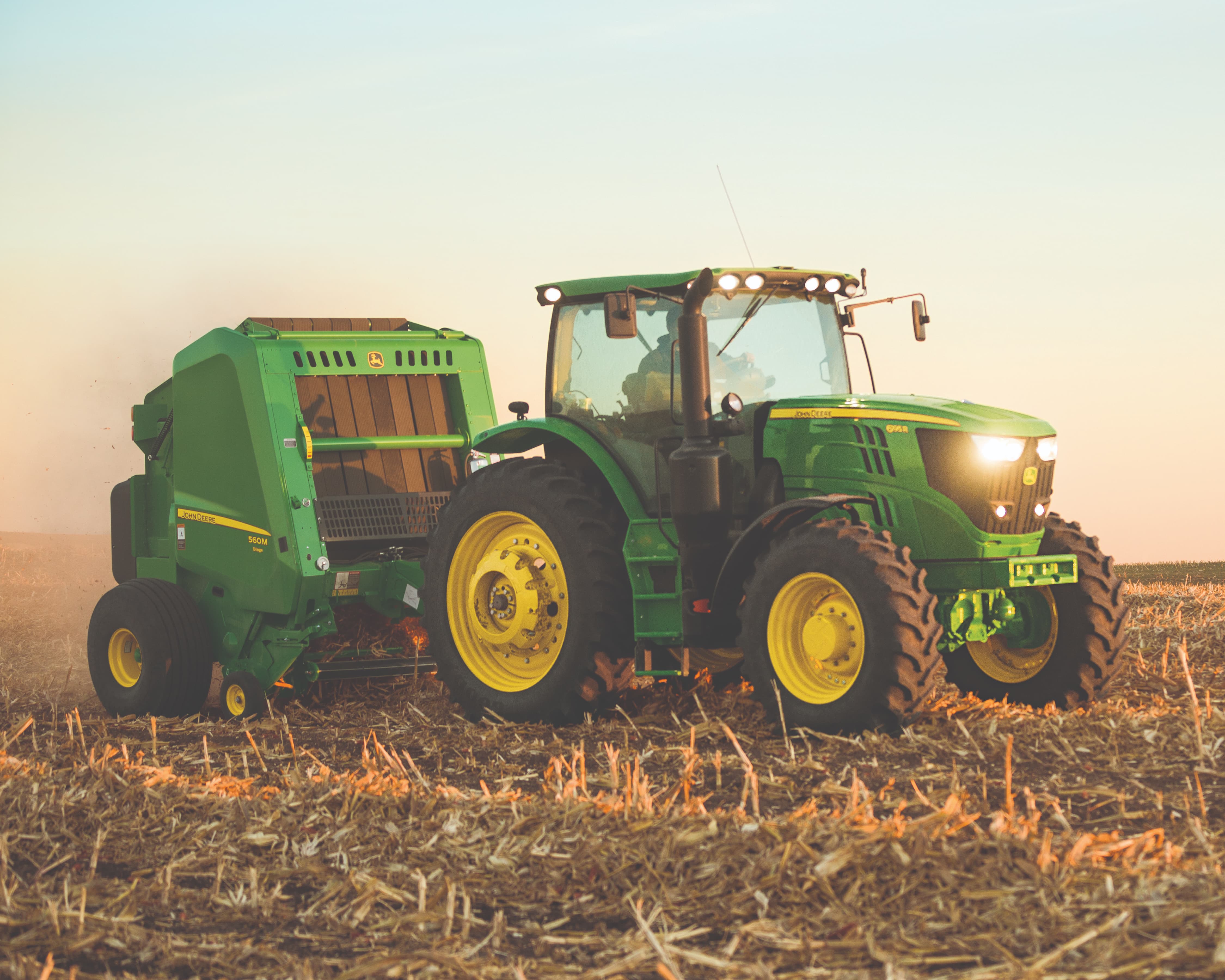 A John Deere round baler and tractor at sunset