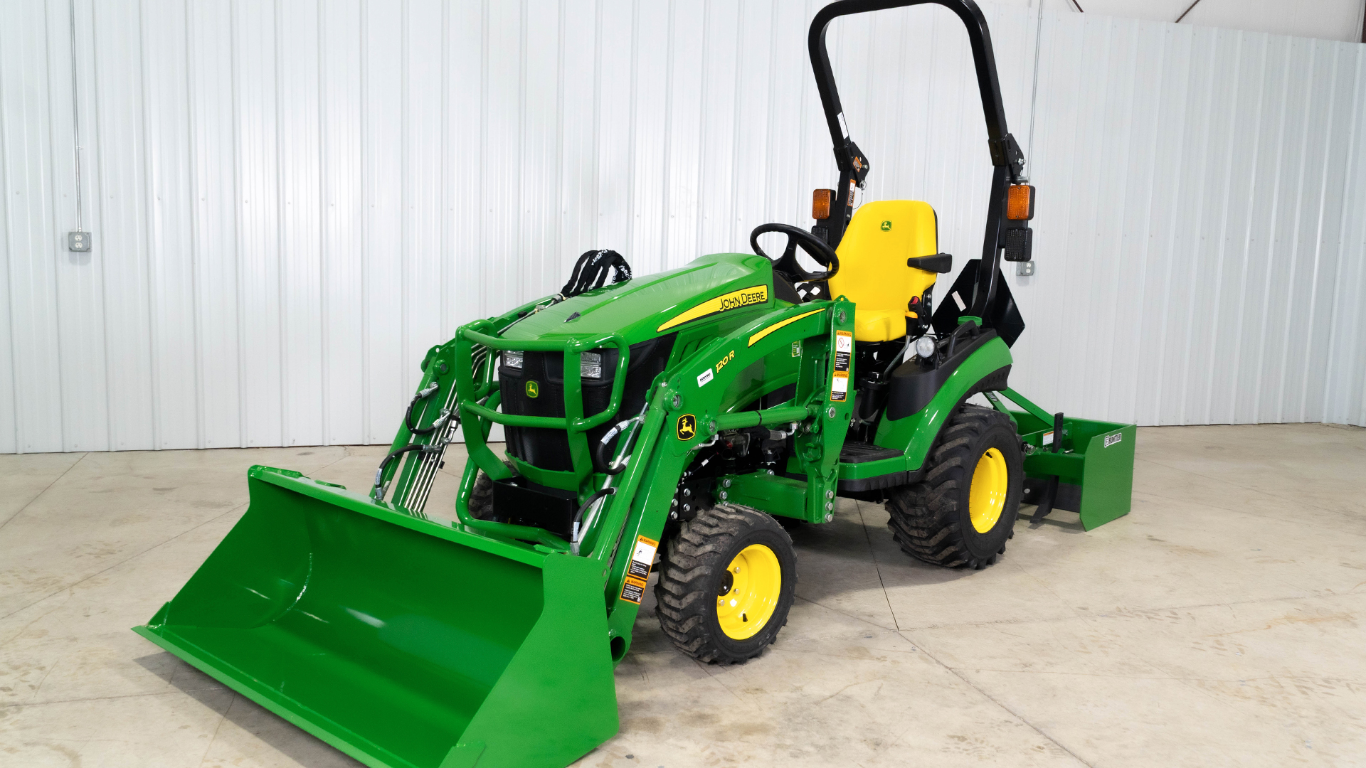 John Deere 1025R compact tractor with a loader grading a gravel driveway