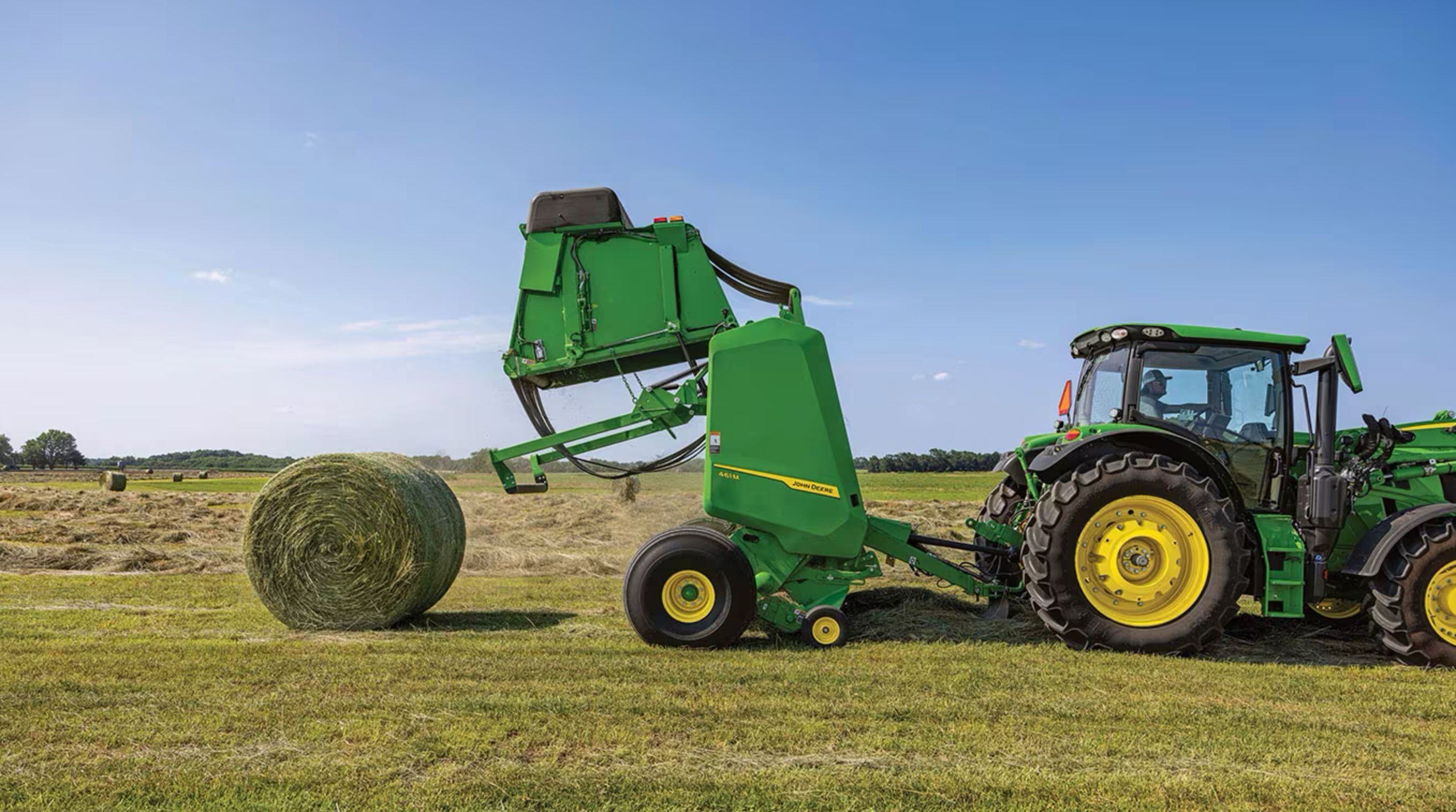 A John Deere round baler and tractor in a hay field