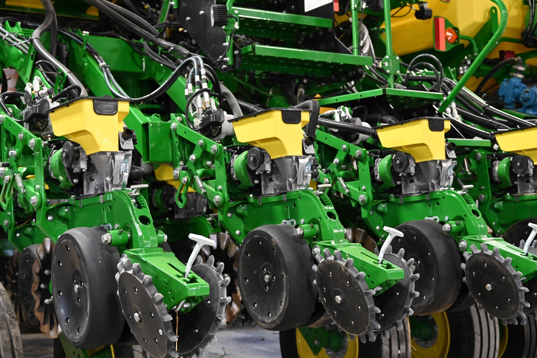 Close-up of several green and yellow John Deere planter row units with seed hoppers and planting mechanisms.