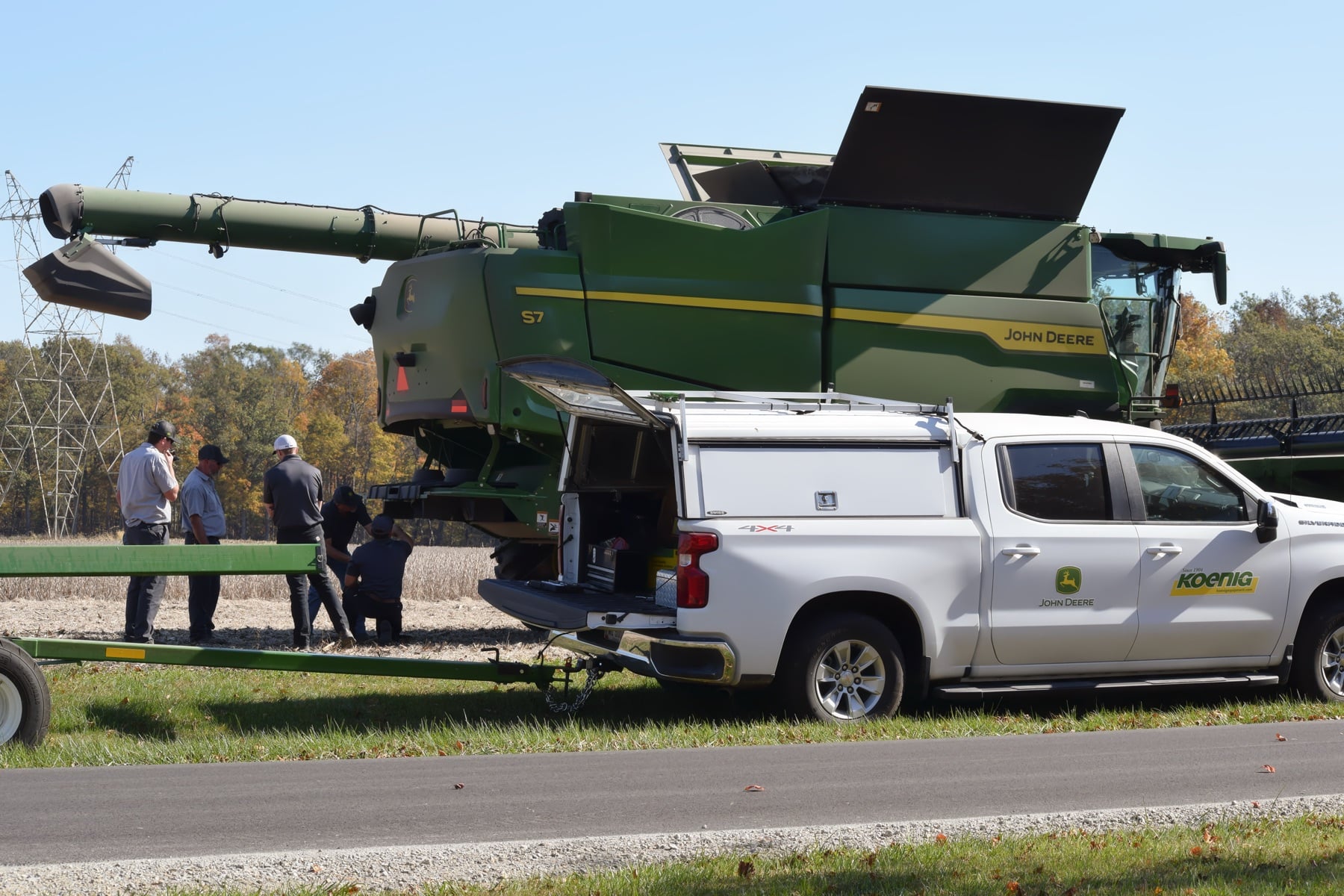 A Koenig Equipment service truck and technicians are with a John Deere combine harvester in a field.