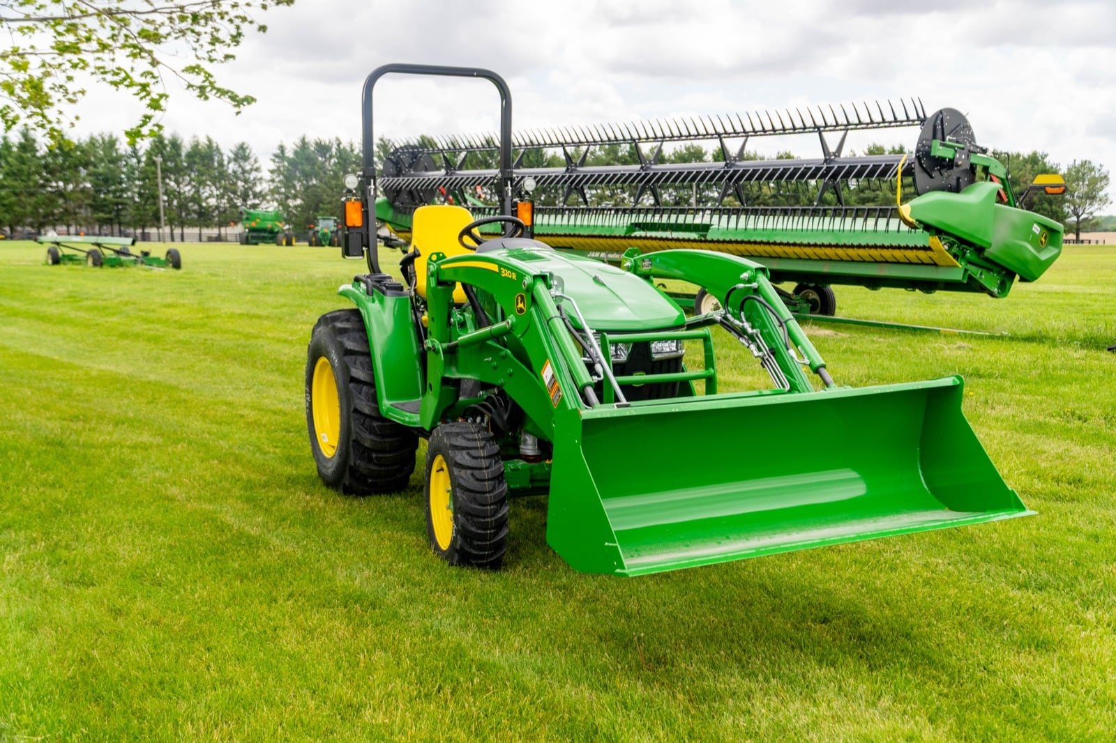 John Deere 3039R with a 320R loader in front of a combine header