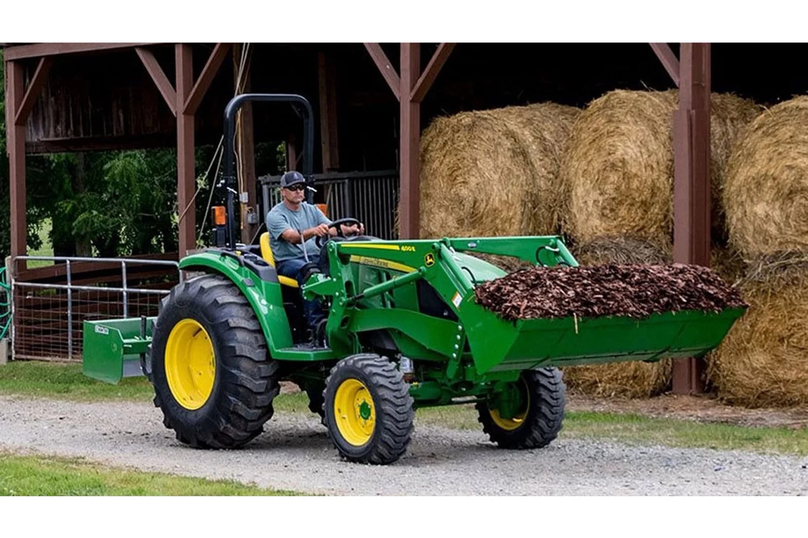 A John Deere 4044M moving mulch by a hay barn