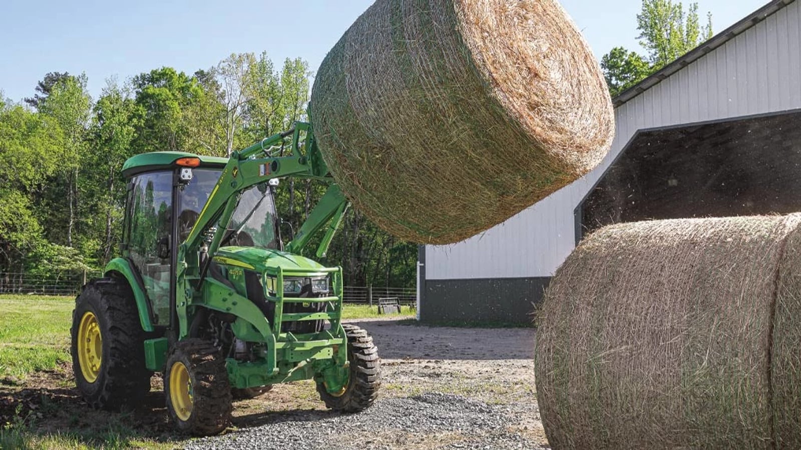 A John Deere 4R tractor lifting a round bale